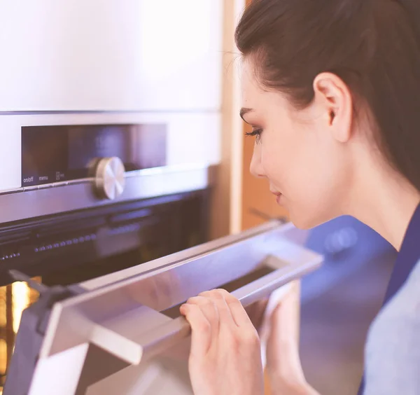 Hermosa joven comprobando cómo le va a su pastel en el horno — Foto de Stock