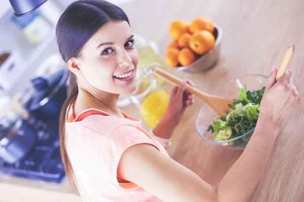 Leende ung kvinna blandar färsk sallad i köket. — Stockfoto