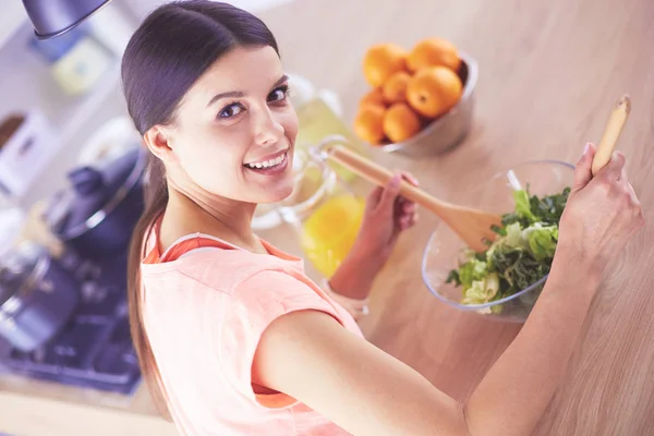 Sorrindo jovem mulher misturando salada fresca na cozinha. — Fotografia de Stock