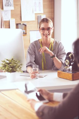 Kadın terzi, dikiş atölyesindeki özel dikim elbise hakkında potansiyel müşteriyle iletişim kuruyor.