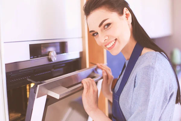 Beautiful young woman checking how her cake is doing in the oven — Stock Photo, Image