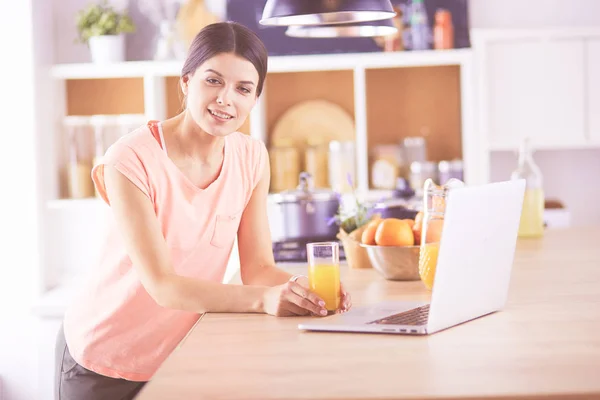 Egy fiatal nő a konyhában laptoppal, aki recepteket keres, mosolyog. Élelmiszer blogger koncepció — Stock Fotó