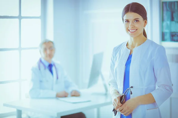 Un médico sonriendo a la cámara con su compañero de sexo masculino en la parte trasera de la sala de consulta en el hospital — Foto de Stock