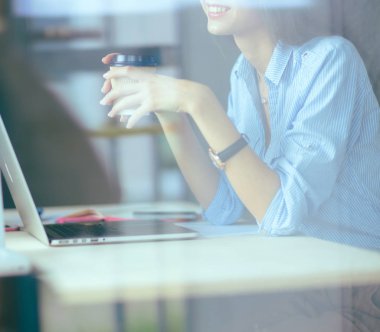 Ofis masasında dizüstü bilgisayarıyla oturan genç bir kadın. Pencereden bakıyor. Genç kadın.