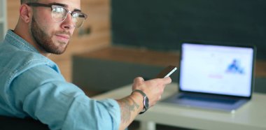 Genç adam kullanarak telefon ve dizüstü bilgisayarda çalışır.