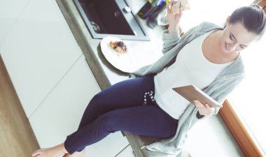 Mutfakta dijital tablet kullanan güzel genç bir kadın..