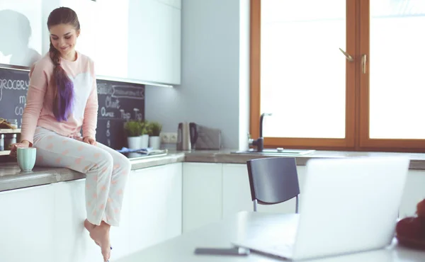 Jonge vrouw zittend op de tafel in de keuken. — Stockfoto