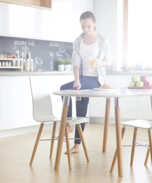 Mujer joven con jugo de naranja y tableta en la cocina. — Foto de Stock