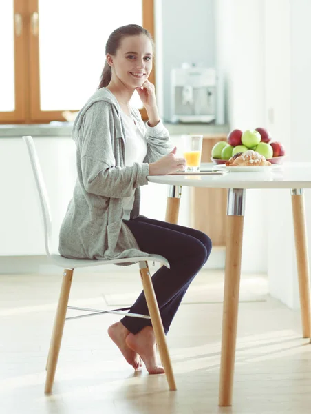 Ung kvinna med apelsinjuice och tablett i köket. — Stockfoto