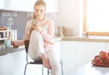 modern mutfakta otururken cep telefonu kullanan kadın.