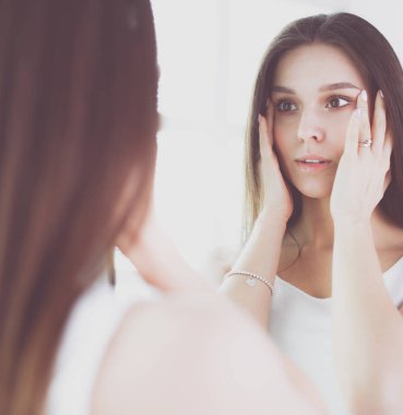 Genç kadın kendini evde aynada yansıma arıyor.