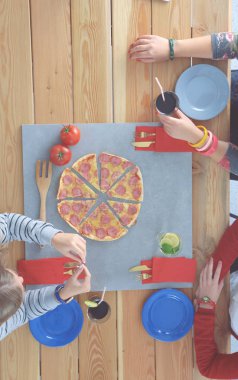 Ahşap masada otururken birlikte yemek yiyen bir grup insanın üst düzey görüntüsü. Masada yemek var. İnsanlar fast food yiyor..
