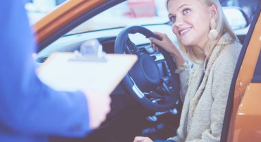 Auto Show 'da yeni bir arabada oturan mutlu genç kadın profesyonel bir satıcı araba hakkında bilgi söyler