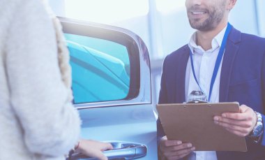 Kadın satıcısı galeride yeni bir arabanın yanında duruyor.