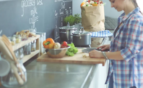 Ung kvinna skära grönsaker i köket nära skrivbordet. — Stockfoto