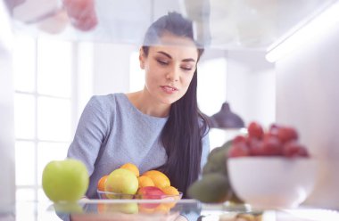 Gülümseyen kadın buzdolabından taze meyve alıyor, sağlıklı yiyecek konsepti.