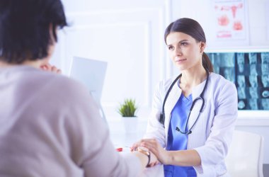 Kadın doktor hastane danışma odasında bir hastayı sakinleştiriyor, elini tutuyor.