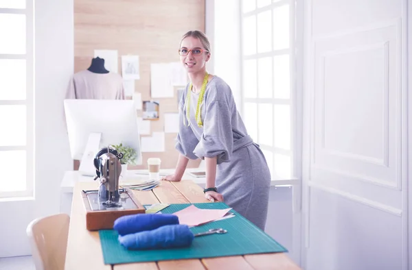 Neue modische Stile schaffen. Fröhliche junge Frau näht, während sie an ihrem Arbeitsplatz in der Modewerkstatt sitzt — Stockfoto