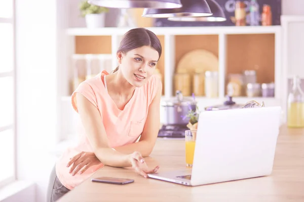 Mulher bonita no telefone usando laptop em casa na cozinha — Fotografia de Stock