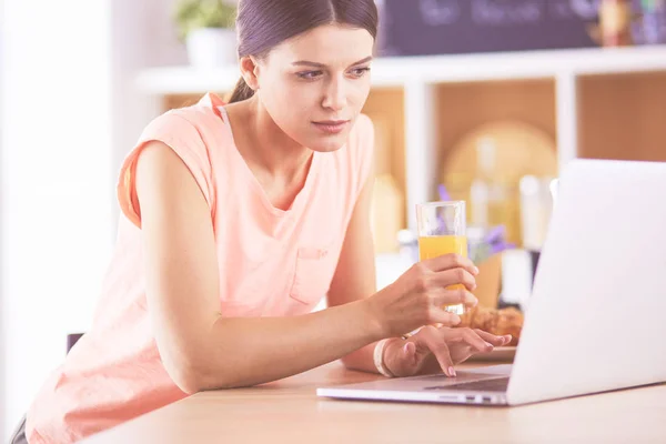 Jonge vrouw in de keuken met laptop computer uitziende recepten, glimlachen. Concept van de voedingsblogger — Stockfoto