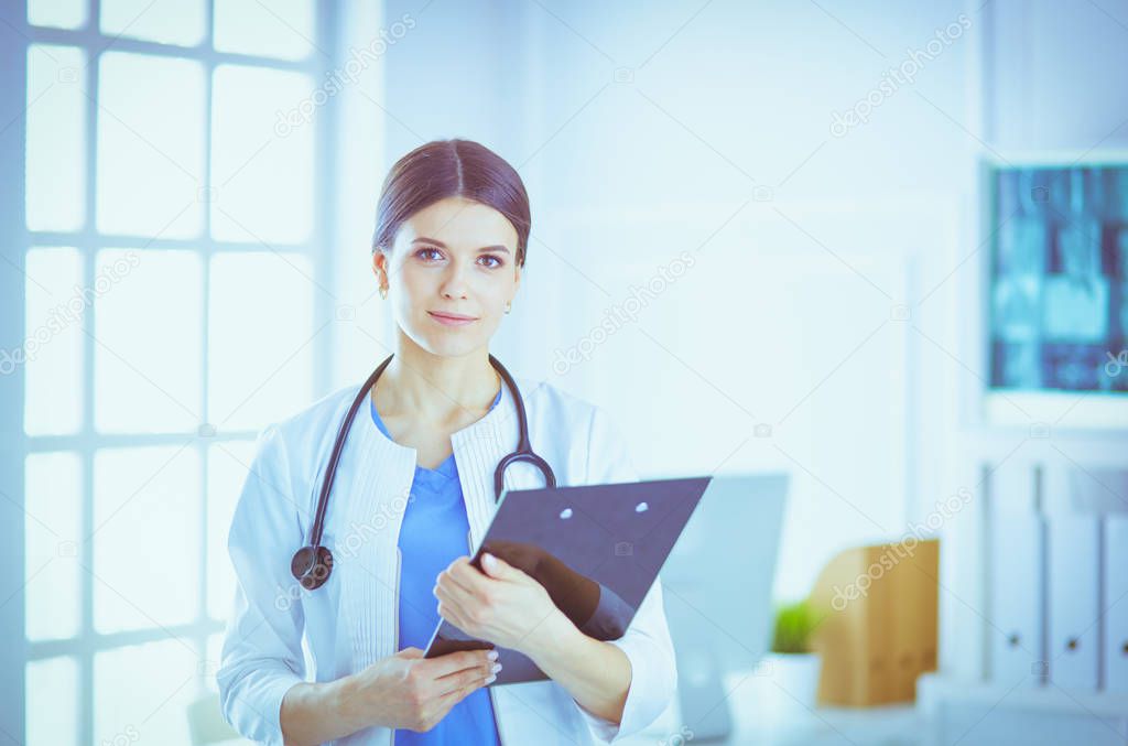Young smiling female doctor with stethoscope holding a folder at a hospitals consulting room