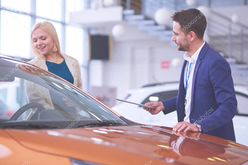 Dealer with woman stands near a new car in the showroom.