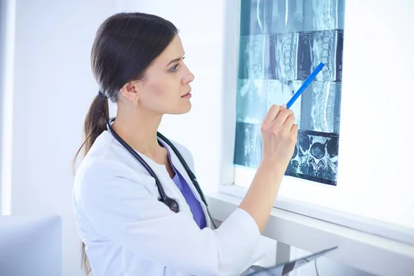 Junge lächelnde Ärztin mit Stethoskop zeigt auf Röntgenbild in Arztpraxis — Stockfoto