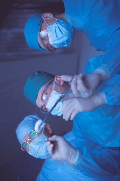 Grupo de cirurgiões no trabalho em sala de operações tonificada em azul. Equipe médica realizando operação — Fotografia de Stock