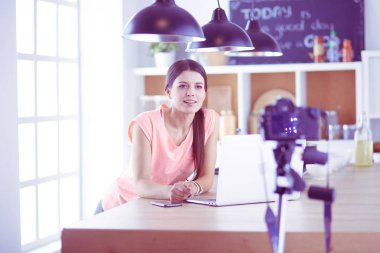 Mutfakta dizüstü bilgisayara benzeyen tariflerle gülümseyen genç bir kadın. Gıda blogcusu kavramı