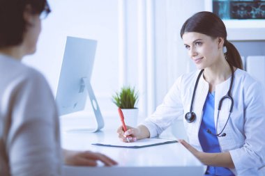 Doktor ve hasta hastane danışma odasında tıbbi sorunları tartışıyorlar. Doktor hasta formunu dolduruyor.