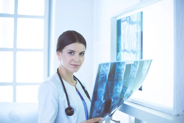 Νεαρή χαμογελαστή γυναίκα γιατρός με στηθοσκόπιο που κοιτάζει ακτινογραφία στο ιατρείο — Φωτογραφία Αρχείου