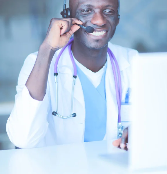 Portrait of young male doctor wearing headset while using computer at desk in clinic. Doctor.