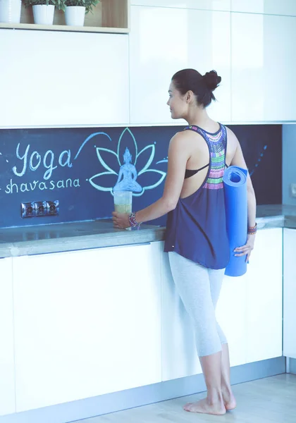 Retrato de una mujer sonriente sosteniendo en su mano una esterilla de yoga mientras estaba de pie en el estudio. Yoga. Una mujer. Bienestar — Foto de Stock