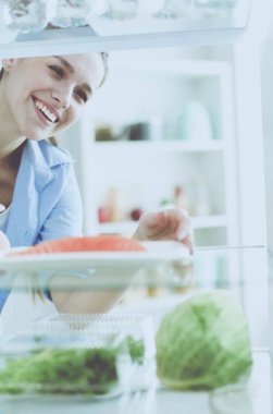 Sağlıklı yiyecek, sebze ve meyvelerle dolu açık buzdolabının yanında duran kadın portresi..