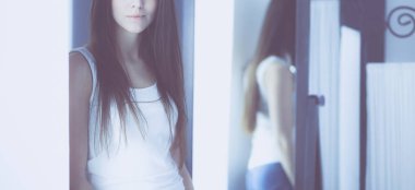 Genç kadın kendini evde aynada yansıma arıyor.