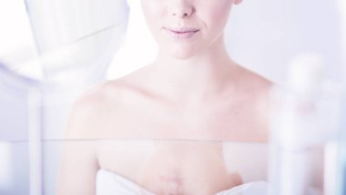 Bornozlu genç kadın banyo aynasına bakıyor.