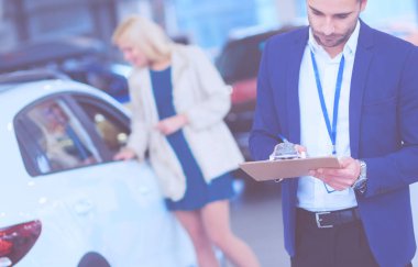 Kadın satıcısı galeride yeni bir arabanın yanında duruyor.