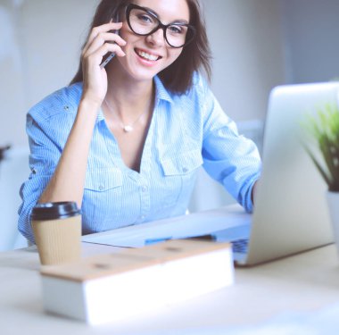 Ofis masasında oturan ve cep telefonuyla konuşan genç ve güzel bir iş kadını. İş kadını