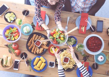 Ahşap masada otururken birlikte yemek yiyen bir grup insanın üst düzey görüntüsü. Masada yemek var. İnsanlar fast food yiyor..