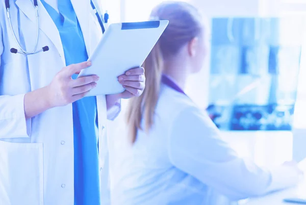 Close up shoot of doctors hands holding tablet and colleague sitting at the table on the background. — Stock Photo, Image