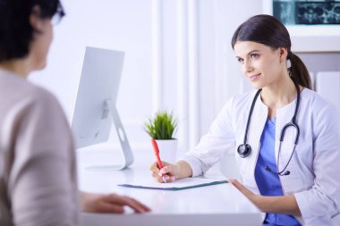 Doktor ve hasta hastane danışma odasında tıbbi sorunları tartışıyorlar. Doktor hasta formunu dolduruyor.