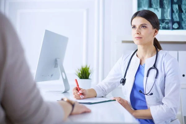 Dokter en patiënt bespreken medische problemen in een ziekenhuis spreekkamer. Doc vult een patiëntenformulier in — Stockfoto