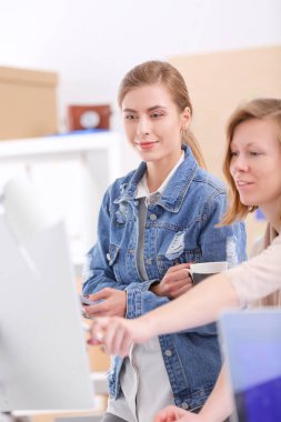 Masanın yanında duran iki genç kadın enstrüman, plan ve dizüstü bilgisayarla.