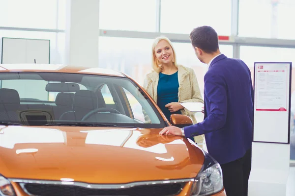 Obchodník se ženou stojí v blízkosti nového auta v showroomu. — Stock fotografie