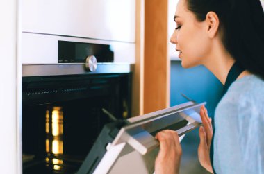 Güzel genç bayan pastasının fırında ne yaptığını kontrol ediyor.