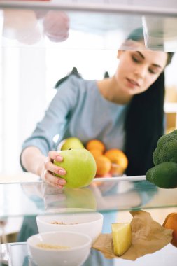 Gülümseyen kadın buzdolabından taze meyve alıyor, sağlıklı yiyecek konsepti.