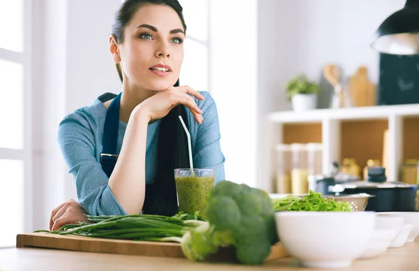 Mujer joven con vaso de sabroso batido saludable en la mesa en la cocina —  Fotos de Stock