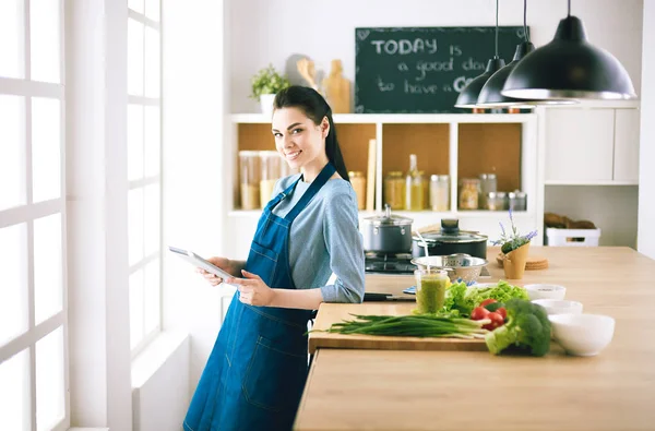 Ung kvinna använder en surfplatta dator för att laga mat i sitt kök — Stockfoto