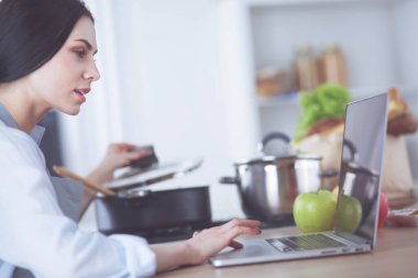 Mutfakta yemek yapmak için tablet bilgisayar kullanan genç bir kadın..