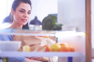 Gülümseyen kadın buzdolabından taze meyve alıyor, sağlıklı yiyecek konsepti.